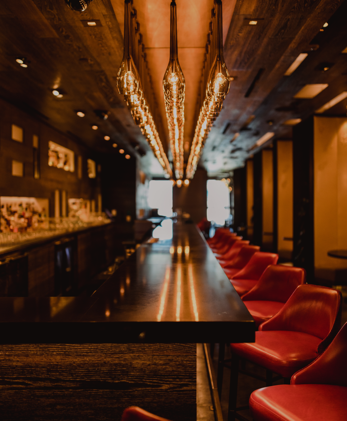 Warmly lit bar counter with red stools and pendant lights